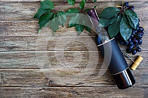 Bottle with red wine, corkscrew, blue grapes, leaves on a wooden table. Wine background with copy space. Top view, flat lay