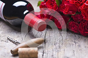 A bottle of red wine, a corkscrew, a gift, a bouquet of red roses on a rustic old vintage background
