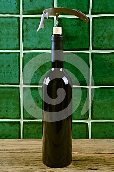 Bottle of red wine with corkscrew over green background.