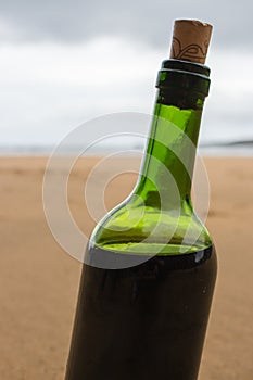 Bottle of red wine on empty beach. Homemade wine in green glass bottle. Full bottle of red wine with cork. Vacation on seacoast.