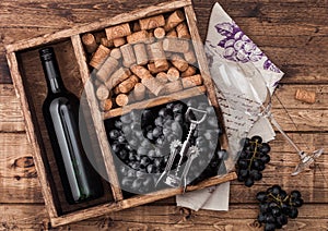 Bottle of red wine and empty glass with dark grapes with corks and opener inside vintage wooden box on grunge wooden background