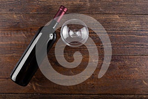 Bottle with red wine and an empty glass, on a wooden background. View from above