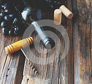 Bottle of red wine with fresh grape and bunch of corks on wooden table