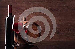 Bottle of red wine, glass and barrel on wooden background