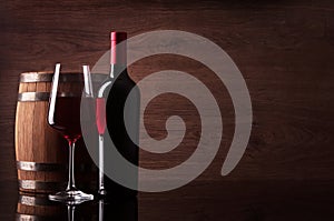 Bottle of red wine, glass and barrel on wooden background