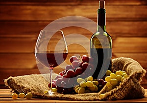 Bottle of red wine, glass and grape in basket in wooden interior