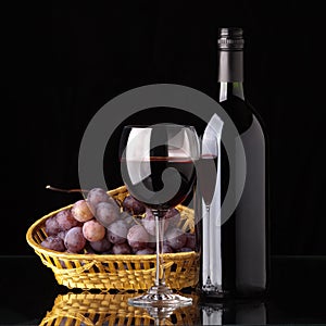 A bottle of red wine, glass and grapes