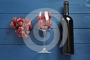 Bottle of red wine, glass and grapes on blue wooden table, flat lay