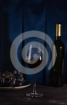 A bottle of red wine, a glass and grapes on a dark background