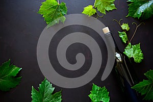 Bottle of red wine, grapes and leaves lying on dark wooden background.