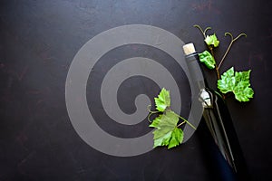 Bottle of red wine, grapes and leaves lying on dark wooden background.