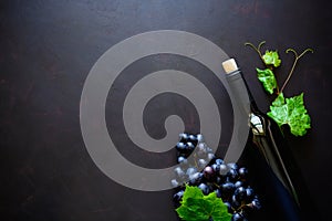 Bottle of red wine, grapes and leaves lying on dark wooden background.