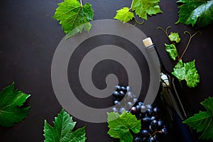 Bottle of red wine, grapes and leaves lying on dark wooden background.