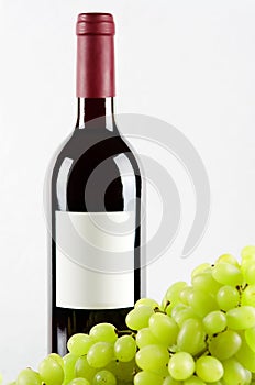 Bottle of red wine and green grapes in front