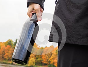 Bottle of red wine in the hands of a man in a black cloak. Men in black cloak provocatively holding a bottle of wine.