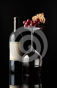 Bottle of red wine and an inverted glass with wine on a black background