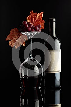 Bottle of red wine and an inverted glass with wine on a black background