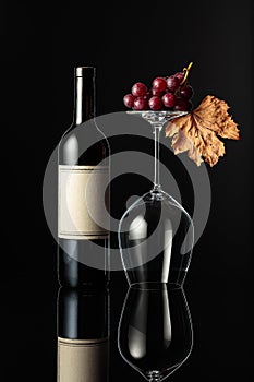 Bottle of red wine and an inverted wine glass on a black background
