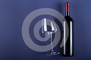 Bottle of red wine without a label and a glass empty on a purple paper background. Mockup drink with place for you label and text