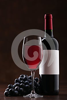 Bottle of red wine with label, glass and ripe grapes