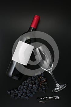 Bottle of red wine with label with glass and ripe grapes on black