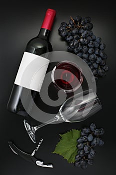 Bottle of red wine with label, glass and ripe grapes on black