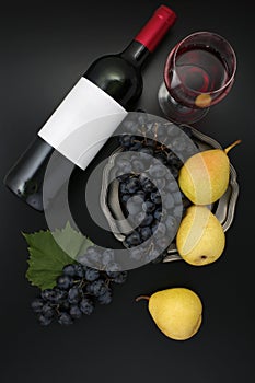 Bottle of red wine with label with glass, ripe grapes and pears