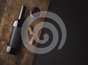 Bottle of red wine with label on old board. Glass of wine and cork. Wine bottle mockup.