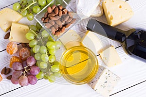 Bottle of red wine with snacks - various types of cheese, figs, nuts, honey, grapes on a wooden boards background