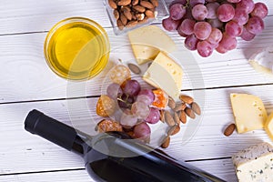 Bottle of red wine with snacks - various types of cheese, figs, nuts, honey, grapes on a wooden boards background