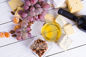 Bottle of red wine with snacks - various types of cheese, figs, nuts, honey, grapes on a wooden boards background