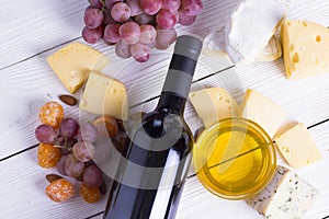 Bottle of red wine with snacks - various types of cheese, figs, nuts, honey, grapes on a wooden boards background