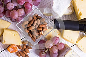 Bottle of red wine with snacks - various types of cheese, figs, nuts, honey, grapes on a wooden boards background