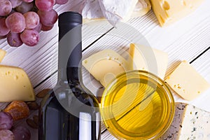 Bottle of red wine with snacks - various types of cheese, figs, nuts, honey, grapes on a wooden boards background