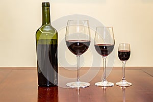 Bottle of red wine with three glasses of different sizes.