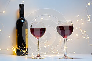 A bottle of red wine, two filled glasses, a bokeh of lights in the background.