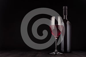 Bottle of red wine and wine glass mock up on elegant dark black wooden background, copy space.