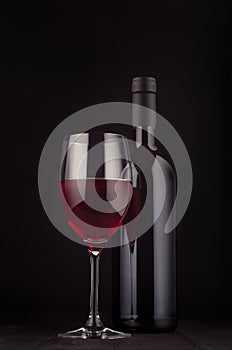 Bottle of red wine and wine glass mock up on elegant dark black wooden background, vertical.