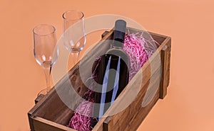 A bottle of red wine in a wooden box and two empty glasses