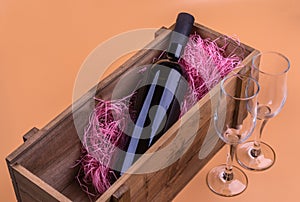 A bottle of red wine in a wooden box and two empty glasses