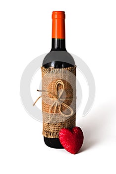 Bottle of red wine wrapped in burlap tied with twine and red heart on white background. Valentine`s Day. Close-up