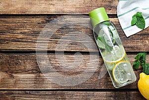 Bottle of refreshing water with cucumber, lemon and mint on wooden table, flat lay. Space for text