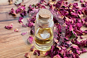 A bottle of rose essential oil with dried rose petals on wooden