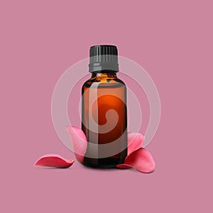 Bottle of rose essential oil and flower petals on dusty pink background