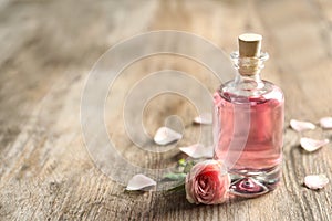Bottle of rose essential oil and flower on wooden table