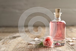 Bottle of rose essential oil and flower on wooden table