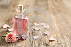 Bottle of rose essential oil and flower on wooden table