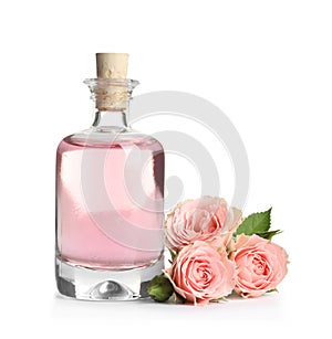 Bottle of rose essential oil and flowers on white