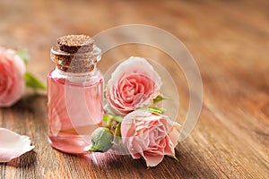 Bottle of rose essential oil and flowers on wooden table, space for