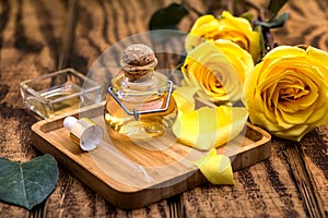 Bottle of rose essential oil and flowers on wooden table, space for text